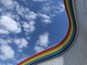 Image of a rainbow wall under a blue, cloudy sky